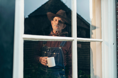 Farmer with hat having a coffee and smoking cigarette while looking out window.の写真素材