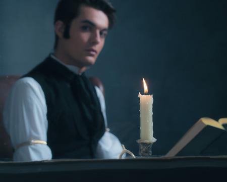 Candlelight by window with blurred retro victorian man reading book.の写真素材