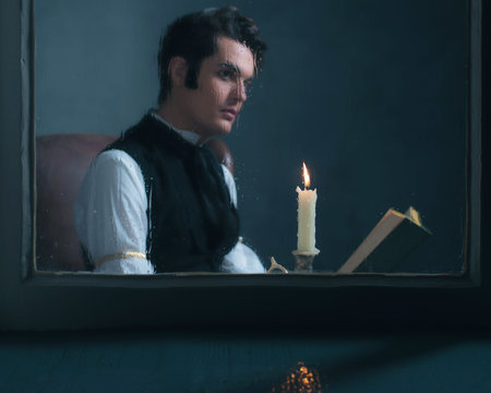 Candlelight behind rainy window with retro victorian man reading book out of focus.の写真素材