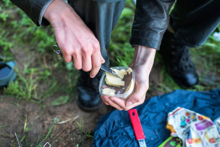 Male hand with knife grabbing butter out of container during hiking trip. Top view.