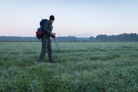 Rear view of hiker in field wrapping up trekking gear. Noordijkerveld. Achterhoek. Gelderland. The...