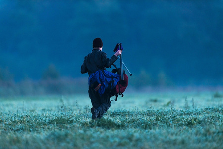 Young man walking with backpack and stool into field at cold morning.の写真素材