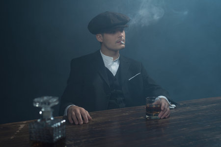 Retro 1920s english gangster sitting at table with whiskey. Peaky blinders style.の写真素材