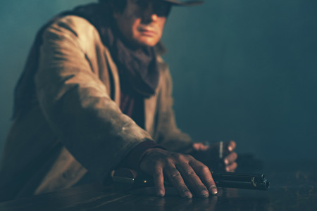 Alert retro late 1960s mexican western actor sitting at bar holding revolver.の写真素材