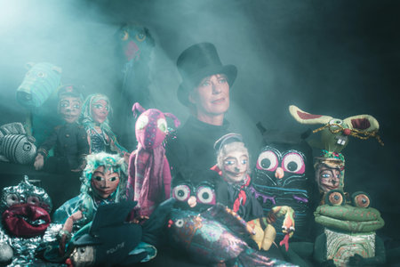 Mystical puppeteer standing between handmade puppets.