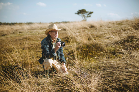 old man sitting with camera in field.の写真素材