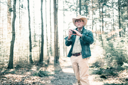 Photographer wearing straw hat and jeans jacket in sunny forest.の写真素材