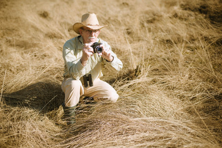 Senior  man with camera in tall grass.