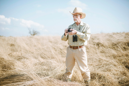 Senior man with camera and binocular in field.の写真素材