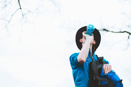 Thirsty hiker drinking from water bottle while standing under tree. Low angle view.の写真素材