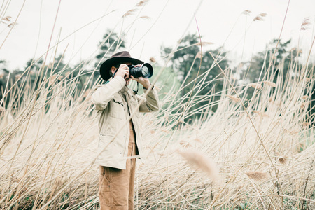 Man with hat standing between reed photographing nature.の写真素材