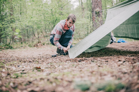 Tourist setting up a tent in spring forest.の写真素材