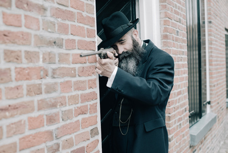 Long bearded man shooting with rifle along wall near front door.の写真素材