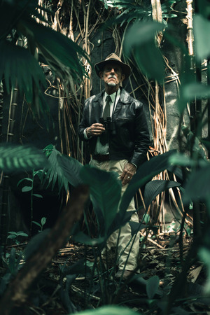 Senior explorer standing in dense jungle looking carefully.の写真素材