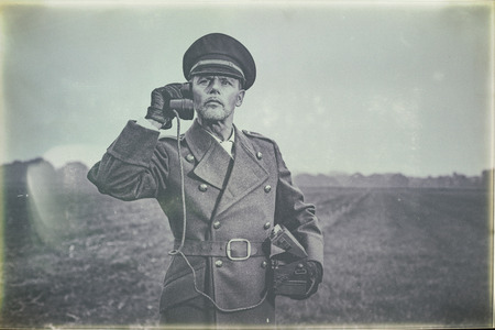 Antique black and white photo of 1940s military officer calling with field phone while standing on farmland.の写真素材