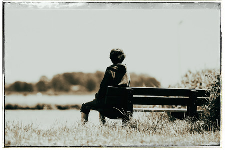 Old fashioned black and white photo of woman sitting on bench looking over water in summertime.の写真素材