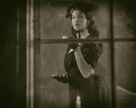 Worn wet plate photo of victorian girl drinking cup of tea behind window.の写真素材