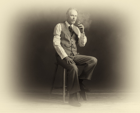 Antique plate photo of cigar smoking vintage 1920s man wearing suit sitting on wooden stool.の写真素材