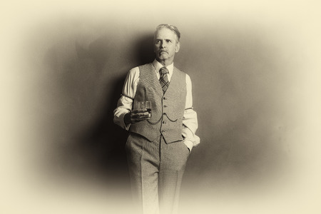Antique plate photo of 1920s businessman with glass of whiskey leaning against wall.の写真素材