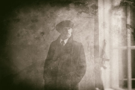 Retro 1920s english gangster wearing flat cap and coat. Standing near window.の写真素材