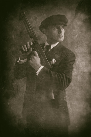 Retro 1920s english gangster wearing flat cap and suit. Standing with gun.の写真素材