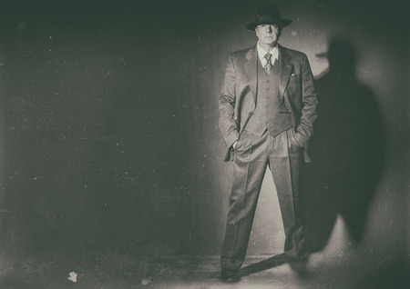 Antique black and white photo of 1940 style gangster standing in front of gray wall.の写真素材