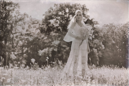 Vintage black and white photo of blonde bride holding white flowers standing in summer field
