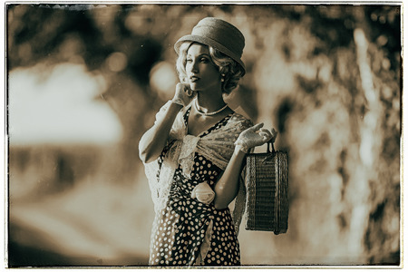 Classic black and white photo of 1930s fashion woman standing with handbag on rural pathway.の写真素材