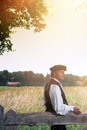 Historical man leaning on wooden fence in countrysideの写真素材