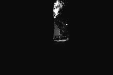 Classic black and white photo of dark forest road with farm at the end.の写真素材