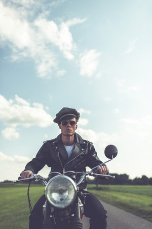 Vintage motorcyclist in sunglasses and cap riding in countryside.の写真素材