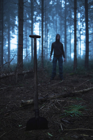 Shovel and man in hoody in spooky misty pine forest.の写真素材
