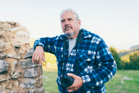 Male tourist with camera leaning against old stone wall. Old Perithia, Corfu, Greece.の写真素材