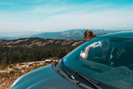 Woman leaning against car reading book in mountains. Sardinia. Italy.の写真素材