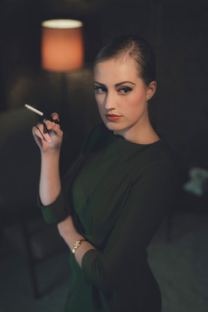 Retro woman in green dress standing with cigarette in hotel room at night.