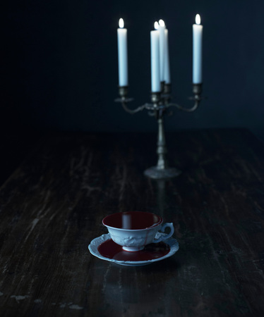 White tea cup in dark blood on dark wooden table with burning candles in candleholder.の写真素材