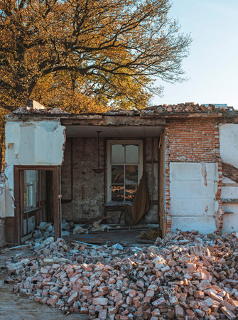 Demolished old farm with living room still standing under autumn tree.