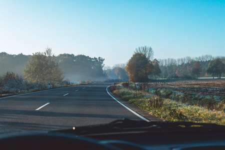 Road in misty rural landscape seen from driver's seat.の写真素材