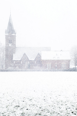 Church in rural landscape covered in snow during snowfall.の写真素材