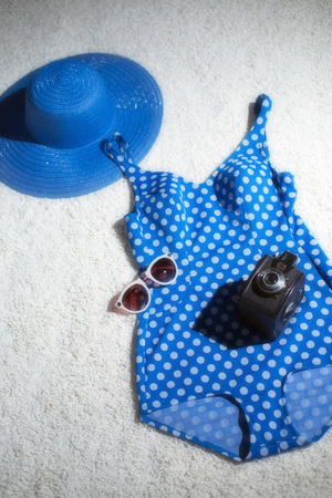 Blue vintage hat with swimsuit, camera and sunglasses displayed on white carpet floor. Top view.の写真素材