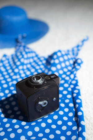 Blue vintage hat with swimsuit and camera displayed on white carpet floor.の写真素材