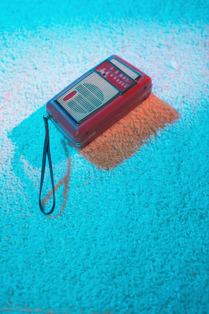 Portable vintage transistor lying on white carpet lit by colored light.の写真素材