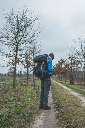 Hiker with backpack standing on dirt road with tire tracks.