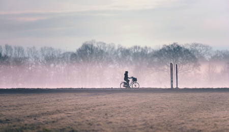 Silhouette of girl cycling on misty country road.の写真素材
