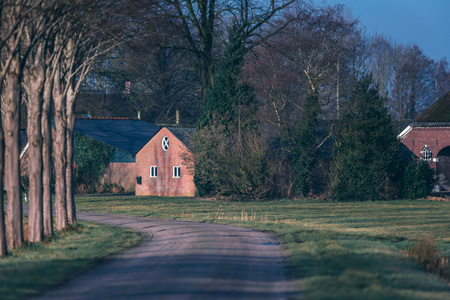 Country road with vintage stone barn lit by morning sunlight.の写真素材