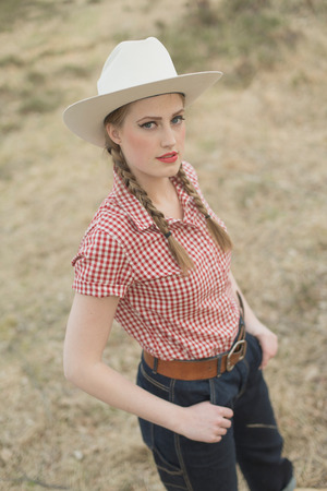 Retro 1950s cowgirl in jeans and checkered shirt in field.の写真素材