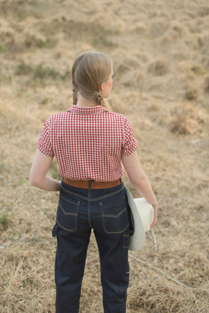 Retro 1950s cowgirl with white hat in red checkered shirt and blue jeans in field. Rear view.の写真素材