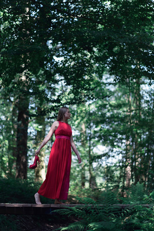 Woman in red dress crossing wooden bridge in summer forest.の写真素材