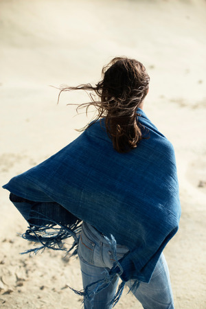 Brunette woman in blue cloth standing in desolate windy landscape. Rear view.の写真素材