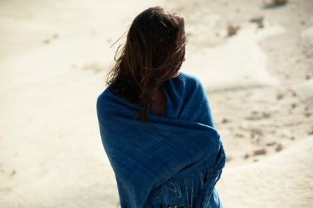 Brunette woman in blue cloth standing in desolate windy landscape. Rear view.の写真素材